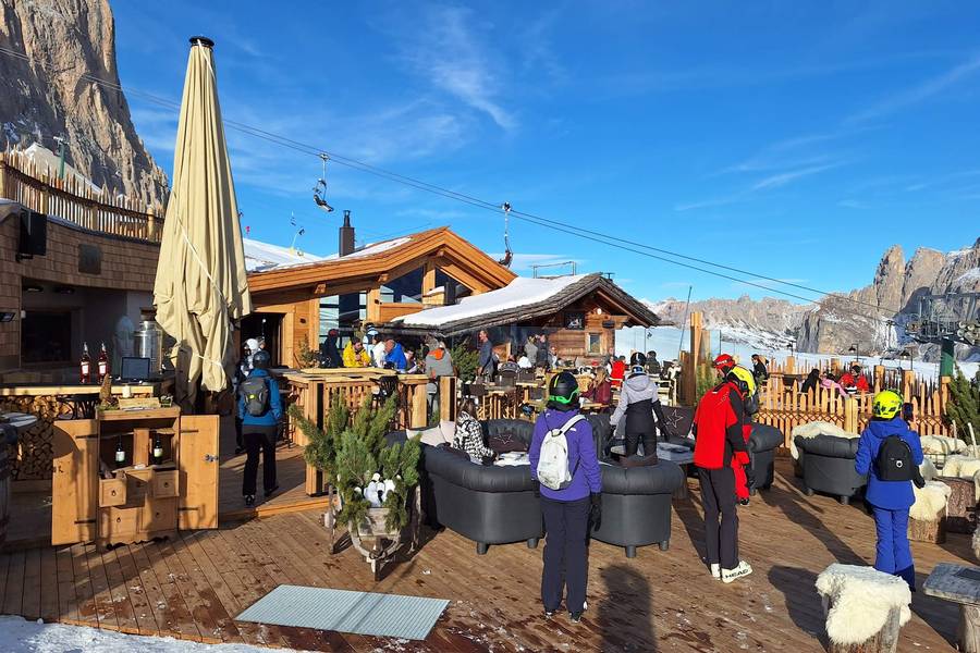 Sunny wooden hut terrace in the Dolomites with a ski lift and rock walls behind