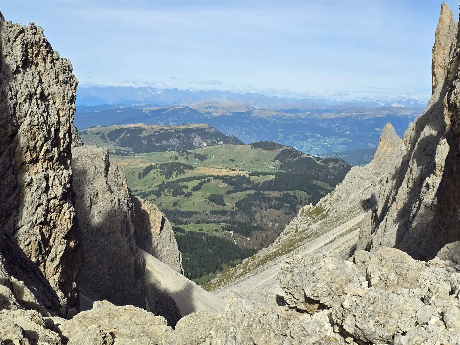 View between two rock towers over green meadows and distant mountains in the Dolomites