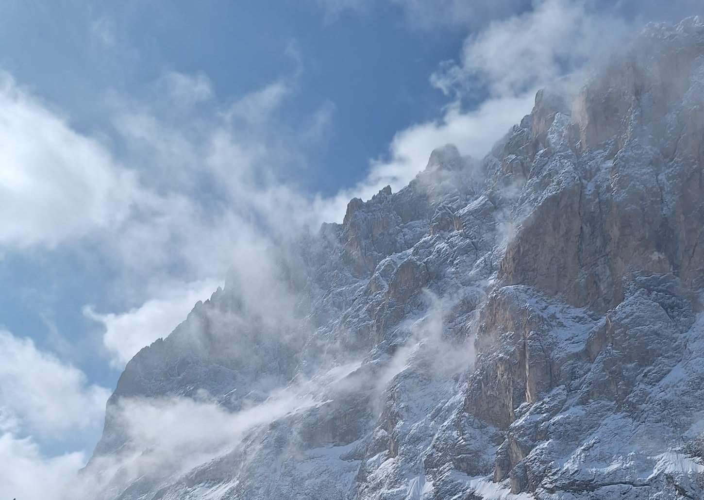 Snow-covered Dolomites rock wall with clouds above a ski slope