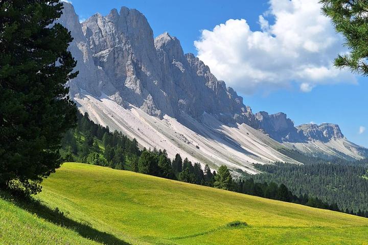 Odle peaks above a green alpine meadow with a hiking path in Val di Funes