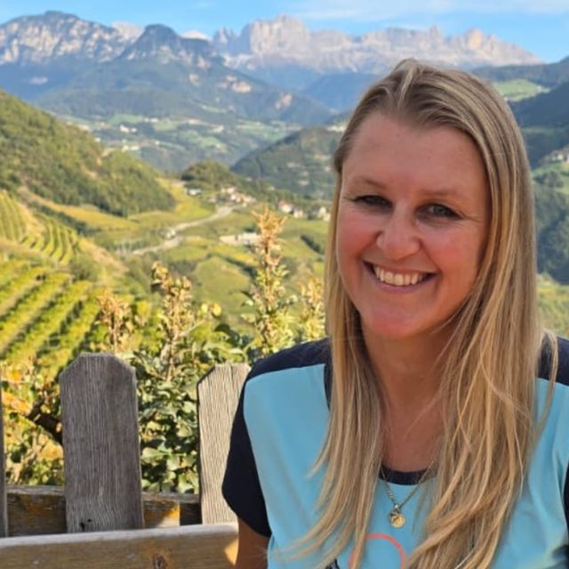 Juli, ski instructor and hiking guide in South Tyrol, smiling in front of vineyards and the Rosengarten mountains