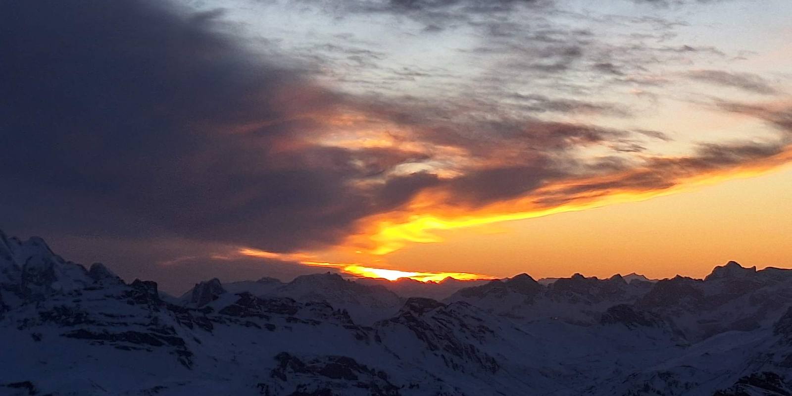Orange sunset between dark clouds above the snow-covered Dolomites peaks