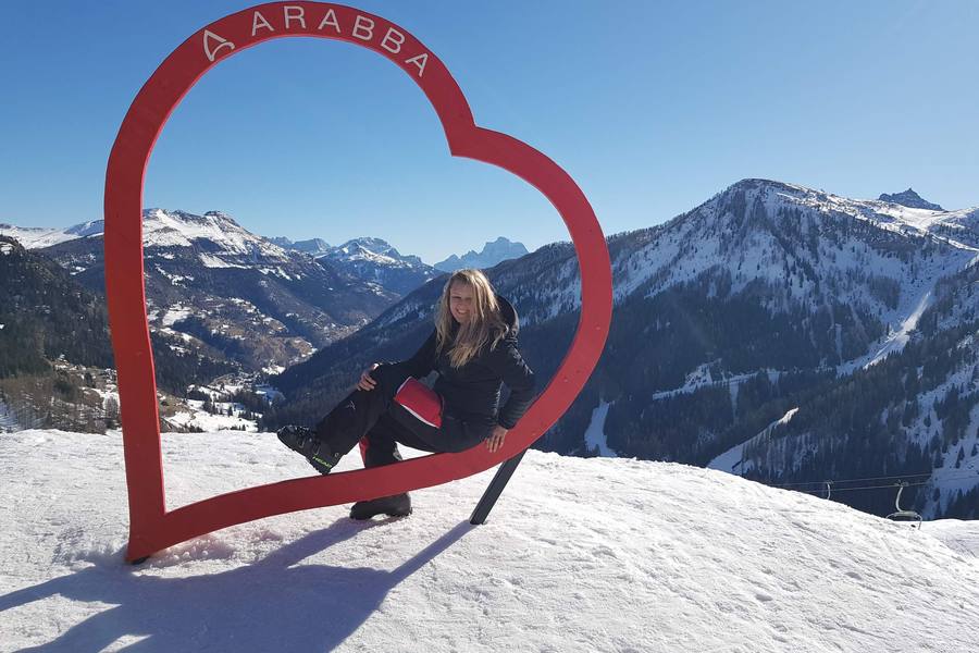 Juli sitting in a red wooden heart frame on a ski slope above the Dolomites