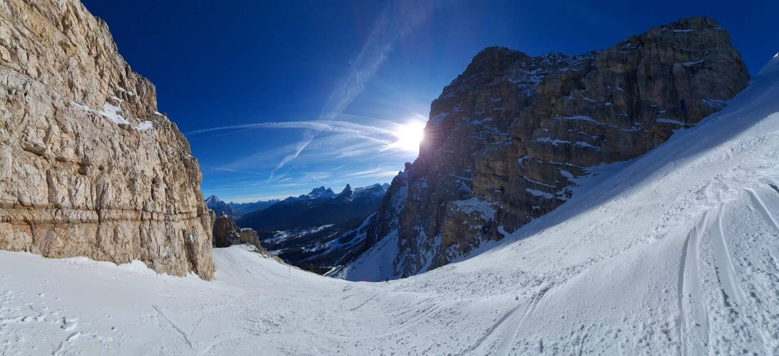Sunlit ski slope between steep Dolomites rock walls